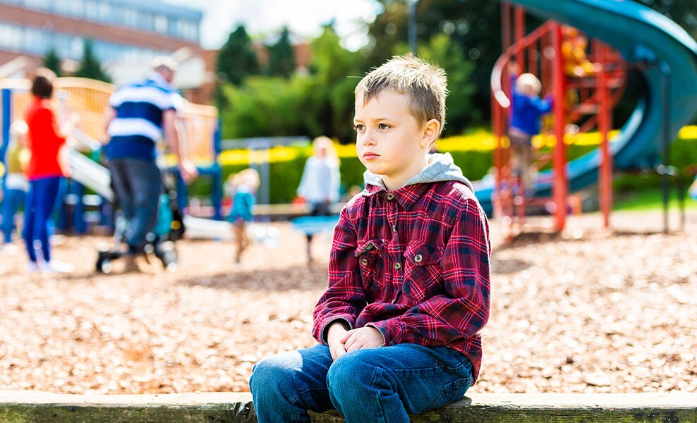 Ein Junge sitzt alleine auf einem Spielplatz