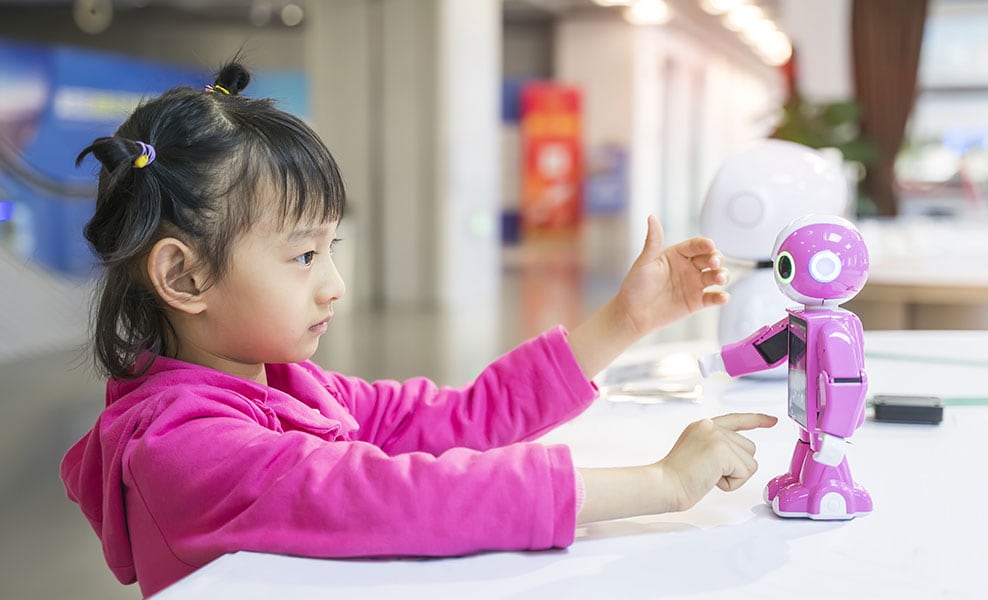 Ein kleines, in Pink gekleidetes Mädchen berührt mit ihrem Finger einen kleinen pinken Roboter